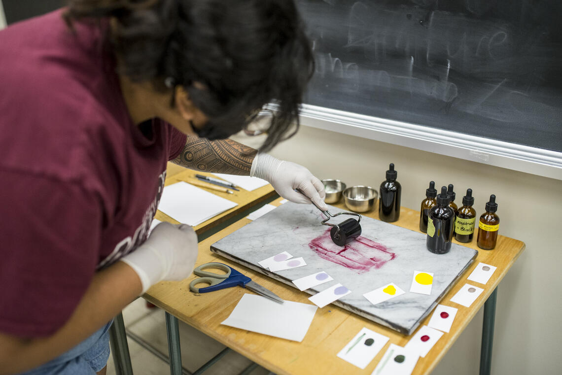 A student leans over and rolls ink on a marble slab in the Book Arts Lab.